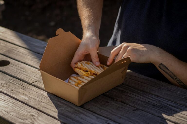 Someone is using a paper food packaging box to pack a sandwich